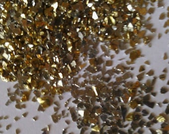 May include: A pile of gold and silver glitter, scattered on a white surface. The glitter is made of small, irregular pieces of metal.