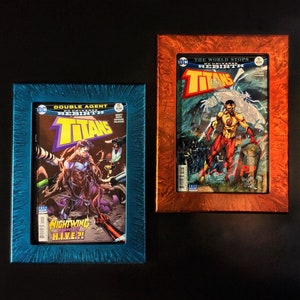 May include: Two framed comic book covers featuring the DC Comics superhero team, the Titans. The cover on the left is blue with the text "Double Agent Rebirth Titans" and features Nightwing. The cover on the right is orange with the text "The World Stops Rebirth Titans" and features a superhero in a red and yellow costume.