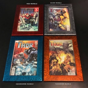 May include: Four comic book frames with different marble finishes. The frames are red, silver, aquamarine, and tangerine. Each frame contains a comic book featuring the character Thor. The comic book titles are "The Unworthy Thor" and "The Mighty Thor".