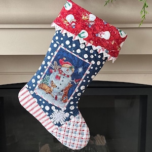 May include: A Christmas stocking with a festive design. The top is red with white snowmen, the body is blue with white polka dots and a central panel featuring a snowman and deer. The toe is plaid, and the cuff is scalloped.