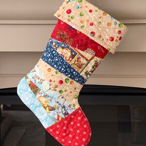 以下が含まれることがあります： 様々なお祝いのパターンが施された、キルト加工のクリスマスストッキング。ストッキングは、雪だるま、鳥、雪の結晶の画像が描かれた赤、青、ベージュの生地を使用しています。カフは、ドット柄のベージュです。