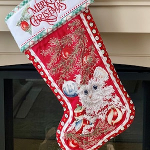 以下が含まれることがあります： 赤と緑のクリスマスストッキングに、青いオーナメントを持った白いネズミが描かれています。ストッキングは白いカフスに赤い糸で「メリークリスマス」と刺繍されています。
