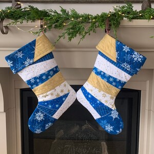 以下が含まれることがあります： 暖炉の上に白いマントルにかけられた、雪片と星の模様の入った青と金のクリスマスストッキング2つ