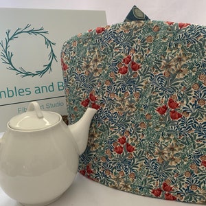 May include: A white teapot with a floral patterned tea cosy. The tea cosy is made of fabric with a blue, green, and red floral pattern. The tea cosy is a great way to keep your tea warm.