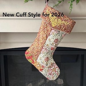 以下が含まれることがあります： 赤、白、緑の花柄のクリスマスストッキング。金色の刺繍入りカフスが付いています。「New Cuff Style for 2026」の文字が見えます。暖炉の前にストッキングが吊るされています。