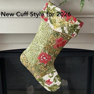 May include: A festive Christmas stocking with a floral design in green, red, and gold. The cuff has embroidered details and the text "New Cuff Style for 2026". The stocking is suspended from a decorative hook.