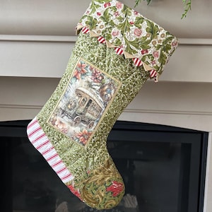 May include: A festive Christmas stocking with a green floral design and a central image of a horse-drawn carriage in a winter scene. The cuff features a floral design with red and white striped trim and decorative bunting.