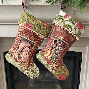 Peut inclure: Deux bas de Noël avec des images religieuses. Les bas présentent un motif floral rouge et or avec une image encadrée d'une scène religieuse. Le haut et le bas des bas ont un motif floral vert. Les bas sont suspendus à une cheminée.