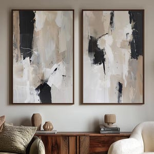 以下が含まれることがあります： 黒、ベージュ、白の筆致が施された2つの額入り抽象画が木製キャビネットの上に飾られています。装飾的なクッションが付いた緑色のソファ、大理石のコーヒーテーブル、クリーム色の肘掛け椅子がリビングルームを完成させています。