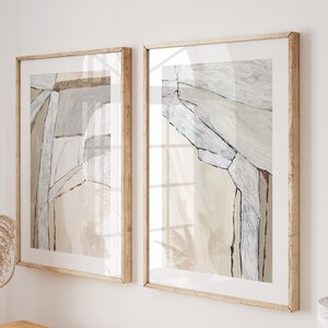 May include: Two framed abstract art prints with neutral tones hang above a wooden console table. The table displays books, a woven basket, and a vase with dried flowers. The room has a warm, inviting aesthetic.