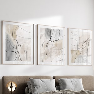 May include: A modern bedroom with a brown upholstered bed with a gray and white patterned throw blanket. Three abstract art prints with black lines and beige backgrounds hang on the wall above the bed.