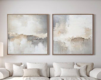 Peut inclure: Deux peintures abstraites dans un salon. Les peintures sont encadrées de bois et présentent un jeu de couleurs beige clair et gris. Les peintures sont accrochées au-dessus d'un canapé blanc avec des coussins blancs. Une table basse en bois se trouve devant le canapé.