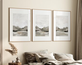 May include: Three framed abstract landscape paintings in muted tones of gray and brown, hanging on a beige wall above a bed with beige linens and pillows.