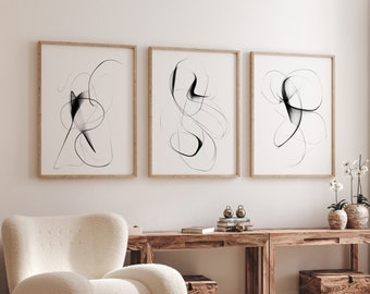 May include: Three abstract line drawings in black and white are framed and hung on a white wall. The frames are made of natural wood. A white armchair sits in front of a wooden table with two matching wooden side tables. A small round wooden table with a book on top sits in front of the armchair.