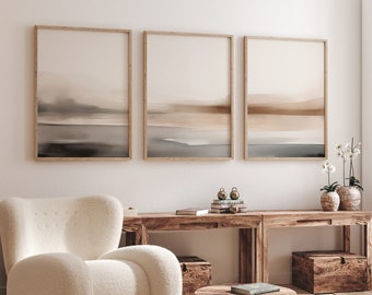 May include: Three framed abstract landscape paintings in muted tones of brown, beige, and gray hang on a white wall above a wooden console table. A white fluffy armchair sits in front of the table, and a small wooden coffee table with a book on top sits in front of the chair.