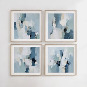 Op de afbeelding: Vier ingelijste abstracte schilderijen in een kleurenschema van blauw, wit en beige. De schilderijen zijn in een rasterpatroon op een witte muur gerangschikt.