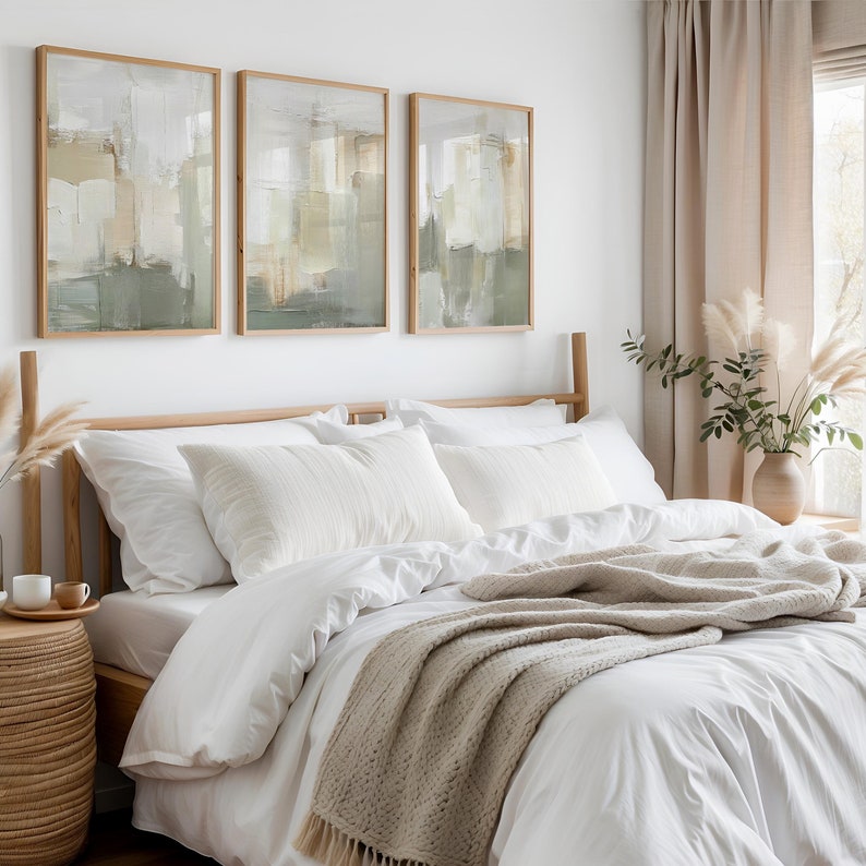 May include: A bedroom with a bed dressed in white linen, pillows, and a beige knitted throw. Three framed abstract art pieces hang above the bed. A woven side table and a vase with pampas grass add to the room's calm aesthetic.
