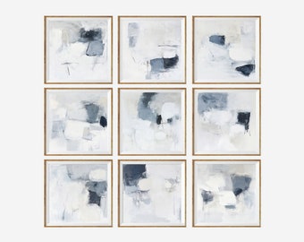 May include: Nine framed abstract paintings in shades of white, grey, and blue. The paintings are arranged in a grid pattern on a white wall.