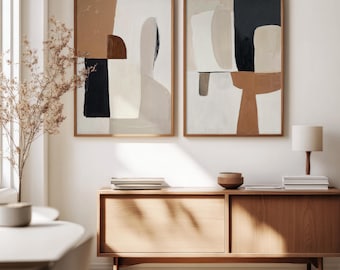 May include: Two framed abstract art prints. The artwork features neutral colors like beige, brown, and black. The frames are made of wood. The prints are displayed above a wooden cabinet with a lamp and decorative items.