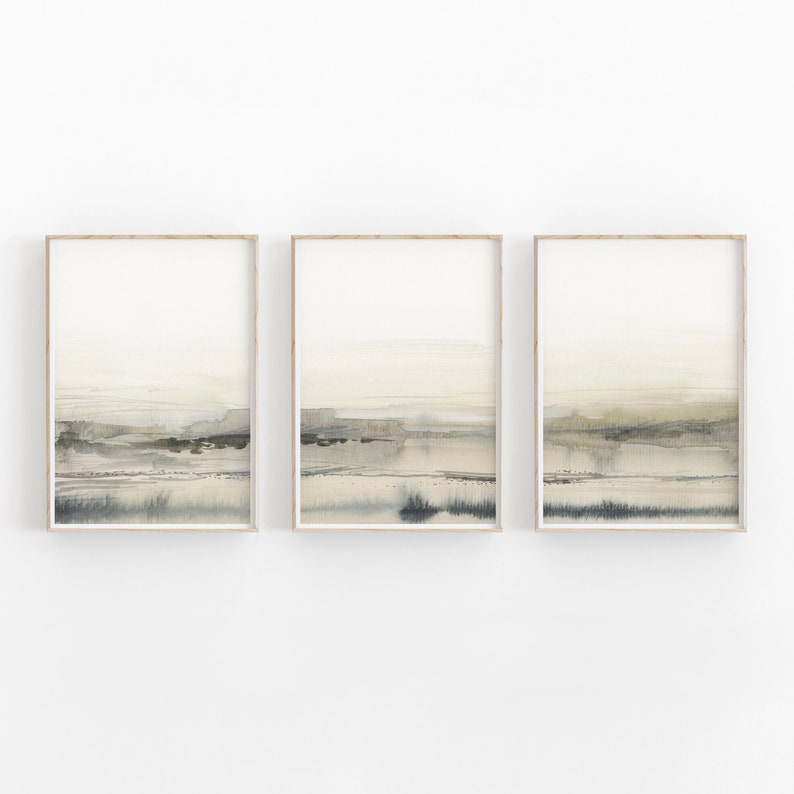 K&ouml;nnte beinhalten: Set aus drei abstrakten Landschaftsbildern in gedeckten T&ouml;nen von Beige, Braun und Grau. Die Bilder sind in einem hellen Holzrahmen gerahmt.