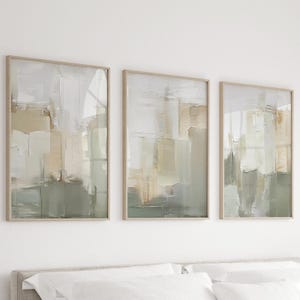May include: Three framed abstract art prints. Each print features a textured, layered design in shades of white, beige, and green. The artwork is encased in a light-coloured wooden frame, creating a cohesive set for wall decor.