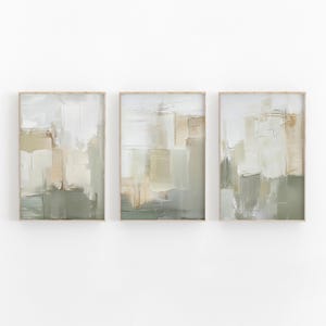 May include: Three framed abstract art prints. Each print features a textured, layered design in shades of white, beige, and green. The artwork has a modern, minimalist aesthetic, suitable for home decor.