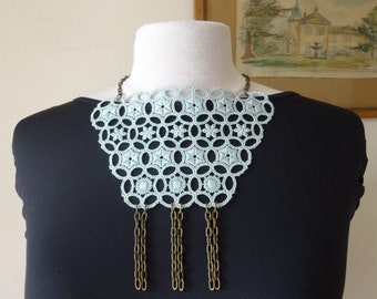 Può includere: Un girocollo in pizzo blu chiaro con un delicato motivo floreale e catene in ottone pendenti.