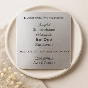 Puede incluir: Una placa cuadrada de metal cepillado que muestra opciones de fuentes para grabado l&aacute;ser y con punta de diamante. La placa presenta el texto "LASER ENGRAVING FONTS" y "DIAMOND TIP ENGRAVING FONTS" junto con nombres de fuentes como "Roustel" y "Rockwell".