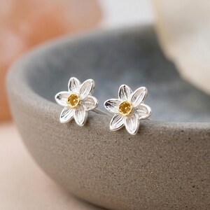 Peut inclure: Une paire de boucles d'oreilles à tige en forme de fleurs à six pétales. Chaque boucle présente des pétales argentés avec une surface texturée et rainurée, ainsi qu'un petit centre circulaire doré en relief. Fermoir à tige classique.
