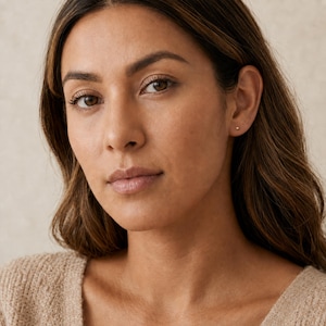 May include: A small, round, metallic stud earring featuring a polished gold-tone finish. The earring is designed as a simple, spherical ball shape that sits flush against the earlobe, providing a subtle and understated appearance for daily wear.