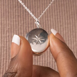 Puede incluir: Un collar con un medall&oacute;n de plata, adornado con un dise&ntilde;o en forma de estrella y una peque&ntilde;a piedra transparente en el centro.