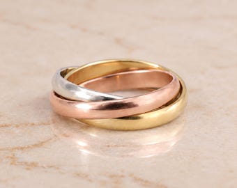 May include: A tri-color interlocking ring featuring three smooth, polished bands in yellow gold, rose gold, and silver tones. The three distinct metal bands are looped together to form a single cohesive piece of jewelry with a rounded profile.