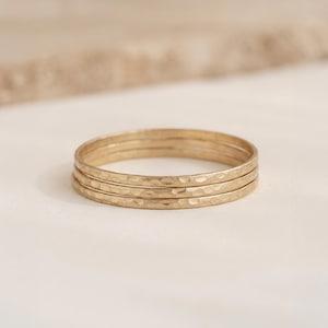 May include: A set of three thin, gold-coloured metal rings stacked together. Each ring features a textured, hammered surface that creates a series of small, reflective indentations along the entire circumference of the bands.