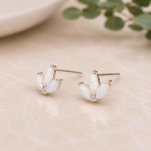 Può includere: Un paio di orecchini a lobo in argento con tre pietre di opale bianco iridescente a forma di pera. Gli orecchini hanno un design floreale delicato e sono montati su perni d'argento. Le pietre di opale brillano di colori.