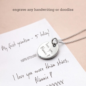 Puede incluir: Un collar con colgante de plata con un dije redondo grabado. El dije presenta el mensaje manuscrito "love you, Nannie P." El fondo incluye texto manuscrito en un papel blanco, con las palabras "engrave any handwriting or doodles" en la parte superior.