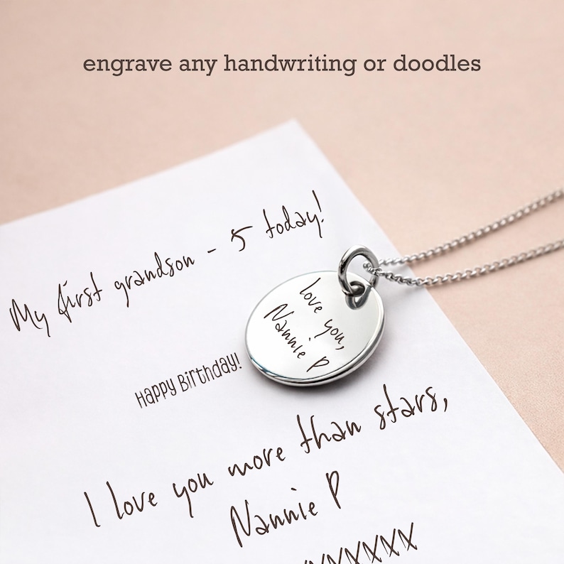 Puede incluir: Un collar con colgante de plata con un dije redondo grabado. El dije presenta el mensaje manuscrito "love you, Nannie P." El fondo incluye texto manuscrito en un papel blanco, con las palabras "engrave any handwriting or doodles" en la parte superior.