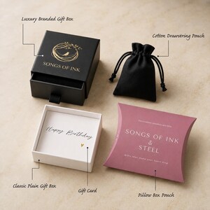 May include: A black sliding gift box with a gold bird logo and Songs of Ink text, a black cotton drawstring pouch, a white gift box containing a Happy Birthday card with a small heart, and a mauve pillow box labeled Songs of Ink & Steel.