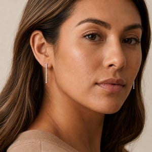 May include: A pair of silver-toned linear drop earrings featuring a vertical row of small, round, clear stones. Each earring consists of a single, slender metal bar set with multiple sparkling gems that hang straight down from the earlobe.