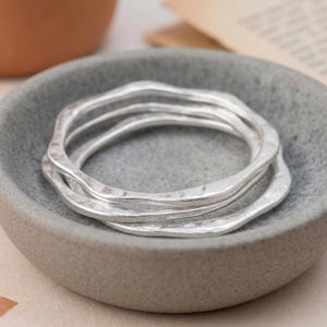 Op de afbeelding: Een set van drie zilverkleurige armbanden met een golvende, onregelmatige en gehamerde textuur. De armbanden hebben een doorlopende, organische vorm met een matte afwerking en zijn gestapeld voor een gelaagd uiterlijk met een metaalglans.