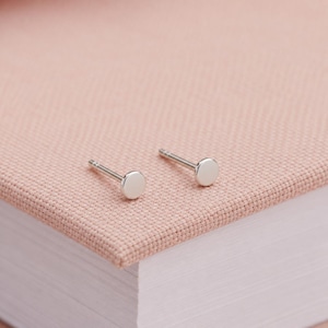 May include: A pair of silver-toned stud earrings featuring a simple, flat, circular disc design. Each earring consists of a smooth, polished round face attached to a straight metal post, presenting a clean and minimalist aesthetic for everyday wear.
