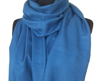 Puede incluir: Una bufanda de pashmina azul sólido con flecos. La bufanda está drapeada sobre un maniquí negro.