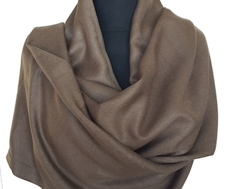 Pode incluir: Um cachecol de pashmina marrom feito de tecido macio e leve. O cachecol está drapeado sobre um manequim e está dobrado de uma forma que mostra a textura do tecido.
