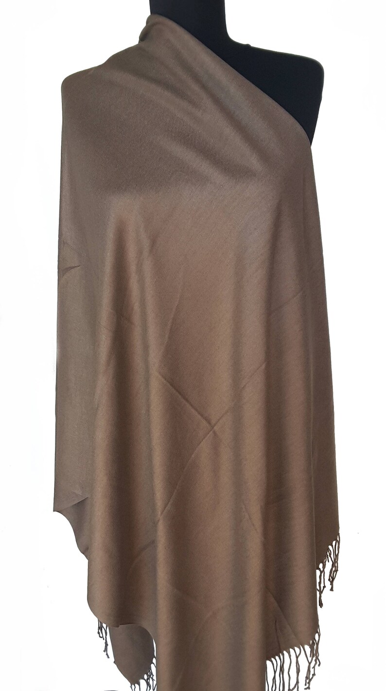 Puede incluir: Un chal de pashmina marr&oacute;n con flecos. El chal est&aacute; hecho de una tela suave y ligera, perfecto para agregar un toque de elegancia a cualquier atuendo.