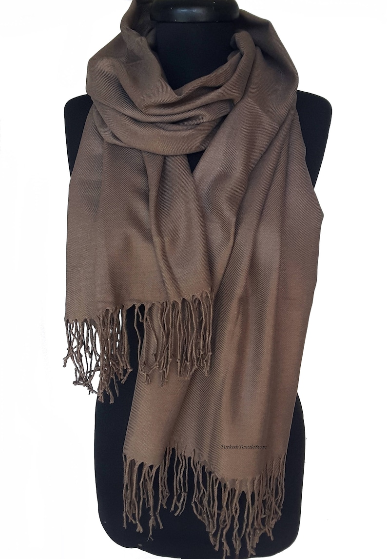 Puede incluir: Una bufanda de pashmina marr&oacute;n con flecos. La bufanda est&aacute; drapeada sobre un maniqu&iacute; negro.