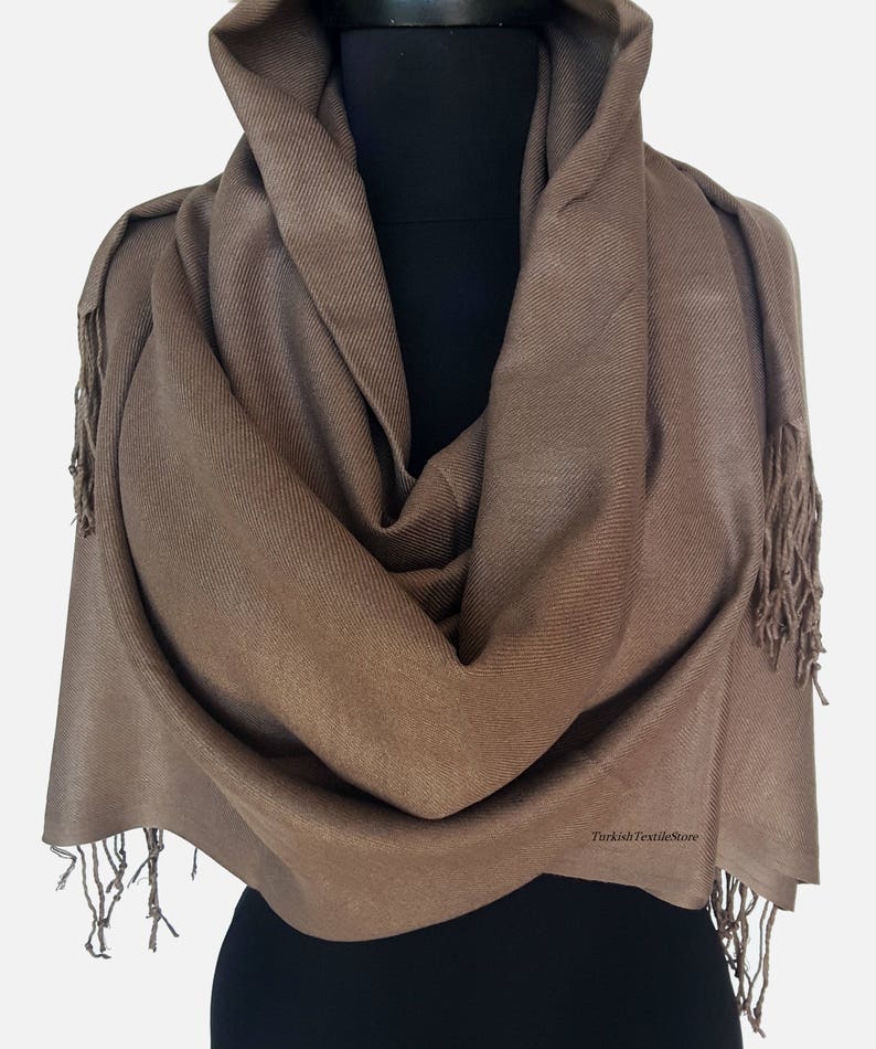 Puede incluir: Un chal de pashmina marr&oacute;n con flecos en los bordes. El chal est&aacute; drapeado sobre un maniqu&iacute;.