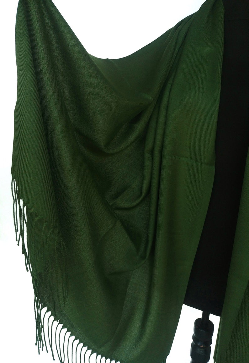 Pu&ograve; includere: Un scialle di pashmina verde scuro con un bordo a frangia. Lo scialle &egrave; drappeggiato su un manichino nero.