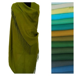 May include: A soft, olive green shawl with fringe. The shawl is folded and draped over a mannequin. A variety of colours of the same shawl are shown in the background.