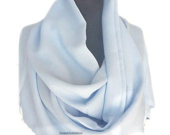 Puede incluir: Una bufanda de pashmina azul claro drapeada sobre un maniquí. La bufanda está hecha de tela suave y ligera con un brillo sutil.