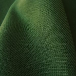 Pu&ograve; includere: Primo piano di un tessuto verde scuro con un motivo testurizzato e tessuto.