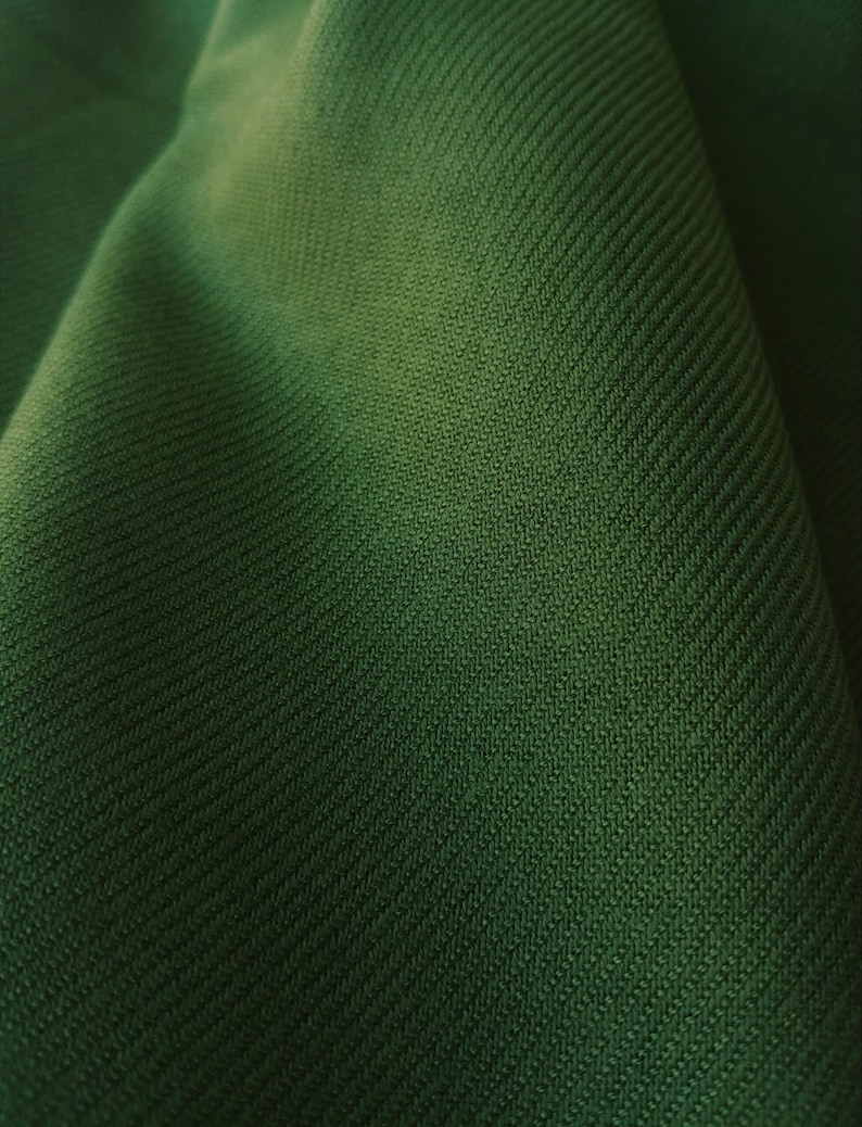 Pu&ograve; includere: Primo piano di un tessuto verde scuro con un motivo testurizzato e tessuto.